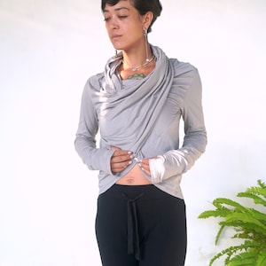 May include: A gray long-sleeved shirt with a cowl neck and thumbholes. The shirt is made of a soft, stretchy fabric and has a relaxed fit.