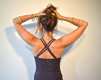 Pode incluir: Uma mulher vestindo um top azul escuro com alças cruzadas e um colar de corrente dourada. Ela está usando pulseiras douradas em ambos os pulsos.
