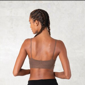 Pode incluir: Suti&atilde; desportivo castanho com al&ccedil;as finas. O suti&atilde; &eacute; usado com cal&ccedil;as pretas. A modelo tem cabelo tran&ccedil;ado. O fundo &eacute; uma parede clara e texturizada.
