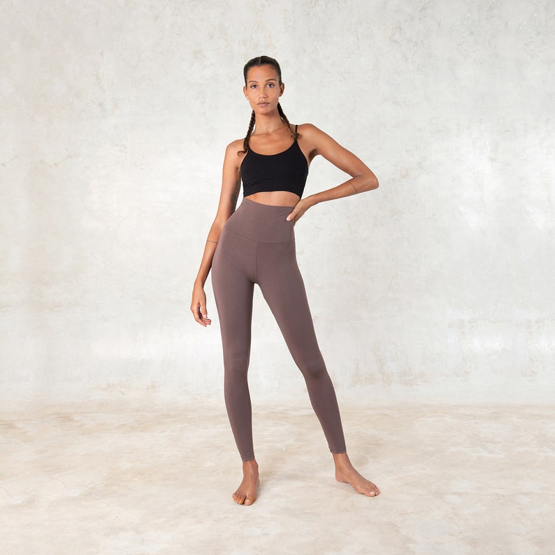 Pode incluir: Uma mulher usando um top esportivo preto e leggings marrons de cintura alta. As leggings s&atilde;o de cor s&oacute;lida e parecem ser feitas de um material macio e el&aacute;stico. A roupa &eacute; adequada para ioga, pilates ou outras atividades f&iacute;sicas.