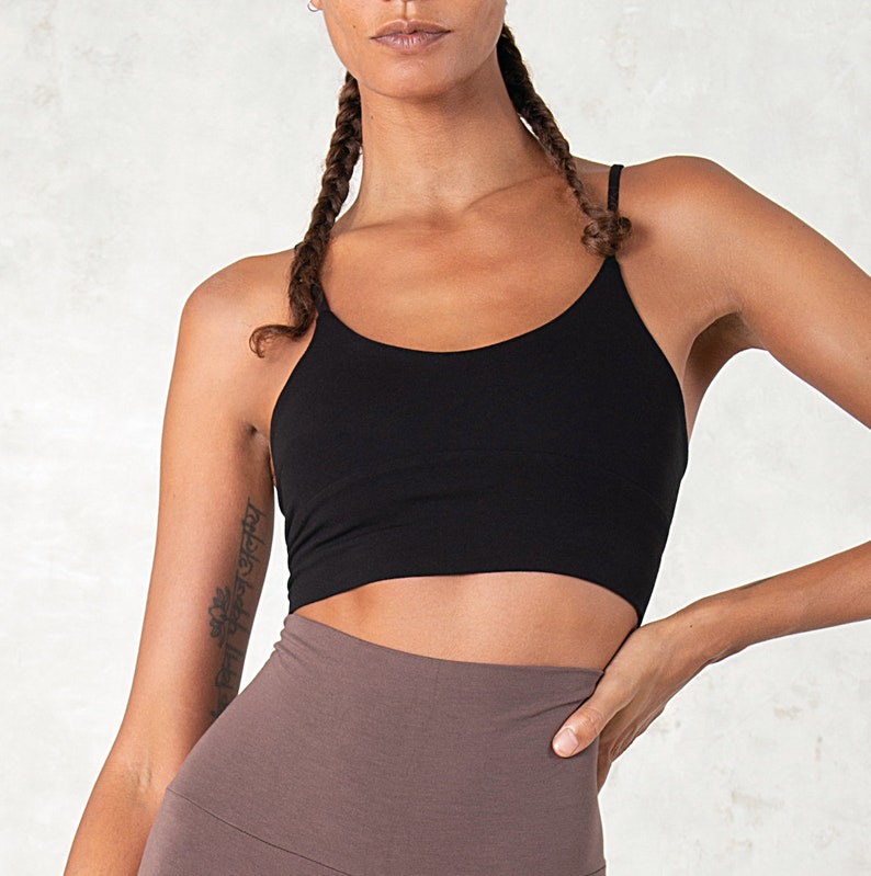 Pode incluir: Um top preto com al&ccedil;as finas. O top &eacute; combinado com leggings castanhas. A modelo tem cabelo comprido tran&ccedil;ado e uma tatuagem no bra&ccedil;o. O fundo &eacute; de cor clara e neutra.