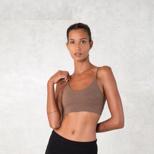 Pode incluir: Um top camisole castanho com al&ccedil;as finas. O top &eacute; combinado com cal&ccedil;as pretas. A modelo est&aacute; em frente a um fundo de cor clara.