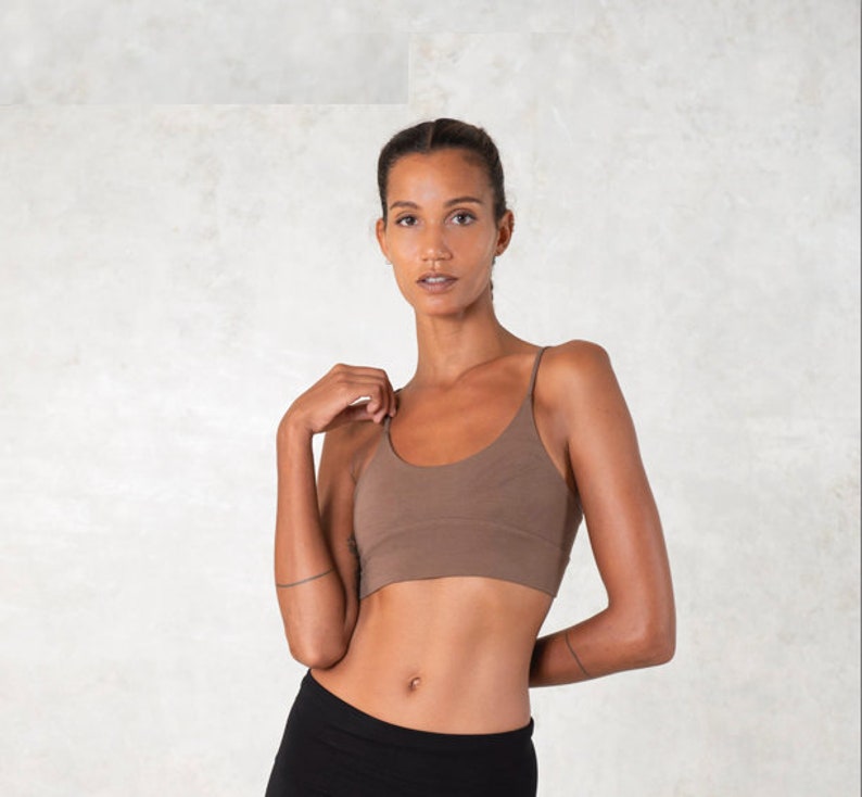 Pode incluir: Um top camisole castanho com al&ccedil;as finas. O top &eacute; combinado com cal&ccedil;as pretas. A modelo est&aacute; em frente a um fundo de cor clara.