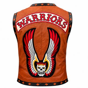 May include: A tan leather waistcoat featuring a large back patch with the text WARRIORS in red letters on a white background. Below the text is a graphic of a white skull with flames and large red, white, and black wings. The waistcoat has black trim.