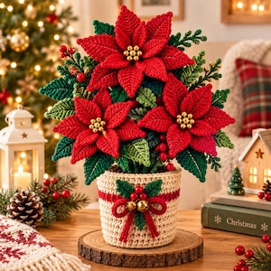 May include: A crocheted poinsettia plant in a beige pot with a red ribbon and gold bells. The plant features vibrant red petals with gold bead centers, surrounded by green leaves and small red berries, all resting on a round wooden base.
