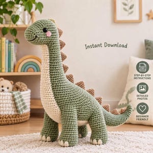 May include: A crochet dinosaur toy made with sage green yarn, featuring a cream-colored belly, small pink cheeks, and a row of brown triangular spikes along its back. The text Instant Download is visible, along with icons for PDF instructions.