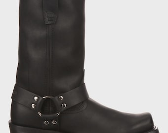 May include: A black mid-calf boot featuring a smooth matte finish, a square toe, and a harness strap across the ankle. The strap is secured with silver-toned metal rivets and a central O-ring. The boot has a low block heel and a pull tab at the top.