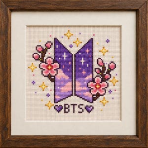 May include: A framed cross-stitch embroidery featuring the BTS logo in purple and pink, surrounded by cherry blossom branches and yellow star accents. The design includes the text BTS flanked by two purple hearts on a cream-colored fabric background.