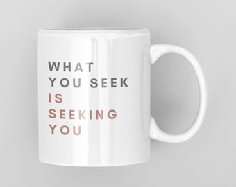 May include: White ceramic mug with a black and rose gold inscription that reads "What you seek is seeking you."