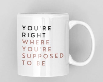May include: White ceramic mug with black text that reads "You're right where you're supposed to be". The text "right" is in black and the rest of the text is in a light brown color.