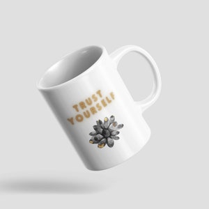 May include: White ceramic mug with a gold design that says "TRUST YOURSELF" and a black and gold flower graphic.