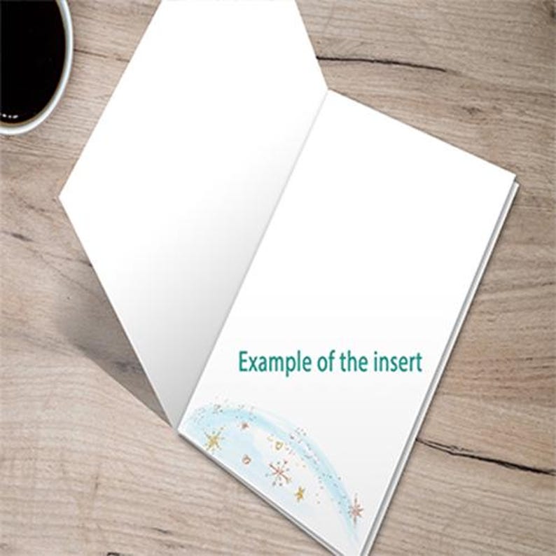 Pu&ograve; includere: Una carta bianca aperta con la scritta "Example of the insert" in turchese. La carta presenta un disegno ad acquerello di stelle blu e oro. Una tazza di caff&egrave; si trova nell'angolo in alto a sinistra. La carta &egrave; su una superficie di legno.