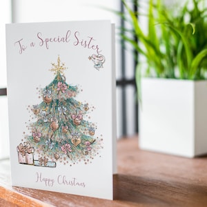 Pu&ograve; includere: Biglietto di Natale con un albero di Natale decorato con palline e fiocchi. La scritta "To a Special Sister" e "Happy Christmas" &egrave; in bordeaux. &Egrave; presente anche un piccolo topo con una stella.