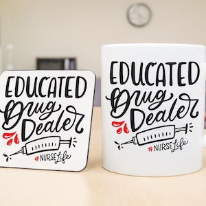 May include: White ceramic mug and coaster set with the text "EDUCATED Drug Dealer" in black script. The design includes a syringe graphic and the hashtag "#NurseLife" in black and red. The coaster is square with rounded corners.