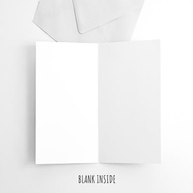 May include: A blank white card with a folded edge, ready for a handwritten message. The card is sitting on a white surface with a white envelope behind it.