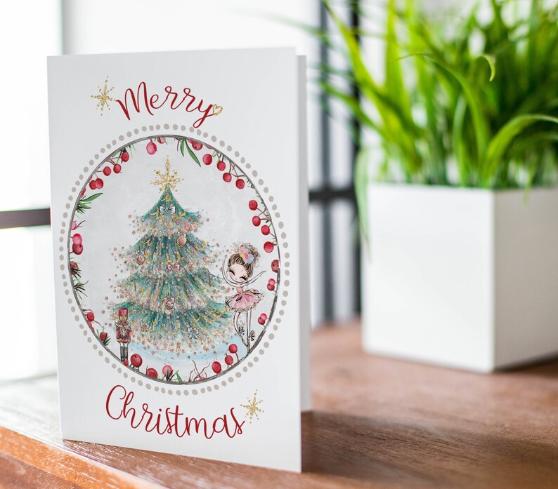 May include: A white Christmas card with a red "Merry Christmas" greeting. The card features a circular illustration of a decorated Christmas tree, a ballerina, and a nutcracker. The illustration is surrounded by a red berry garland.