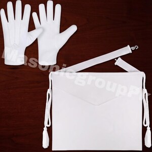 May include: A pair of plain white gloves and a white ceremonial apron featuring a triangular flap, side tassels with braided cords, and an adjustable waist strap with a metal hook closure. The text Masonicgroup is visible in the background.