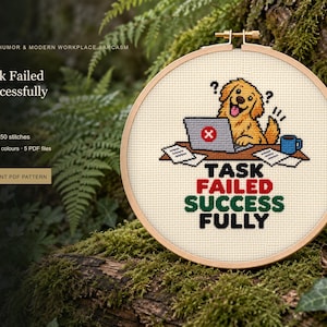 May include: A cross-stitch embroidery in a round wooden hoop featuring a golden dog sitting at a desk with a laptop, a blue mug, and papers. The text reads "TASK FAILED SUCCESSFULLY" in black, red, and green thread against a white fabric background.