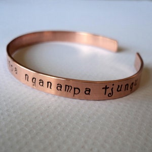 Puede incluir: Una pulsera de cobre con la inscripci&oacute;n "nga nampa tjunga" grabada.