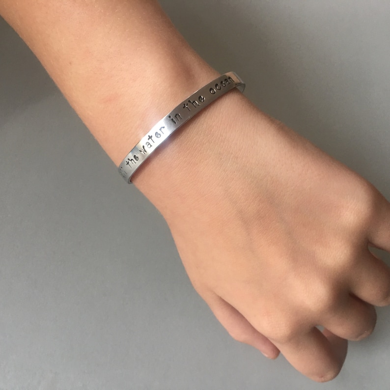Puede incluir: Una pulsera de plata con las palabras "the water in the ocean" grabadas.