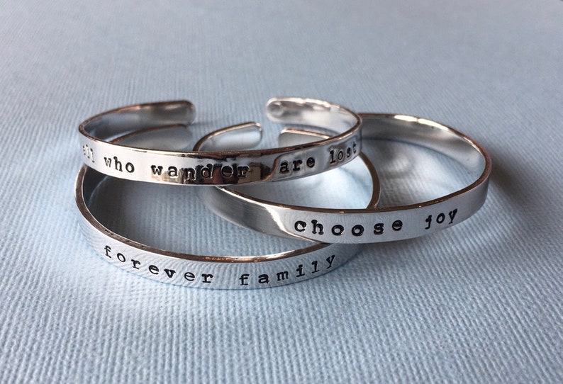 Puede incluir: Tres pulseras de plata con grabados que dicen: "forever family", "who wander are lost" y "choose joy".