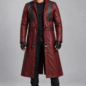May include: A long, deep red leather coat featuring a high collar, black leather accents on the shoulders and chest, silver-toned metal studs, and a waist belt with silver buckles. The coat is worn over a black shirt, black pants, and black boots.