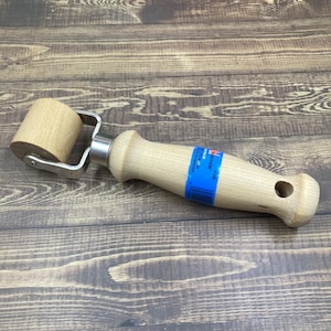 May include: A wooden roller with a metal frame and a wooden handle. The handle has a hole in it and a blue label that says "KREMER - A 20" with a barcode.