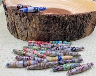 May include: A collection of colorful, handmade paper beads. The beads are made from recycled paper and are strung together to create a necklace or bracelet. The beads are a variety of colors, including red, blue, green, yellow, and orange.