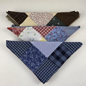 May include: Three triangular fabric bandanas stacked vertically. The top one features brown, cream, and floral patterns. The middle one displays red, white, and blue floral and plaid prints. The bottom one showcases various shades of blue in plaid and floral patterns.