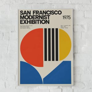 May include: A rectangular exhibition poster titled San Francisco Modernist Exhibition 1975. The design features a large red semicircle, a yellow semicircle, and blue geometric shapes with black vertical stripes on a light beige background.