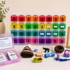 May include: A colorful educational set with a rainbow-colored alphabet organizer, small toys, and flashcards. The set includes 26 letters, word cards, and picture cards. A small pink container holds flashcards with the words "baseball" and "fish".