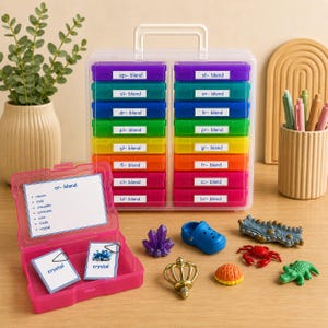 May include: A clear plastic organizer with colorful compartments labeled with word blends. A pink case with flashcards and small toy figures, including a blue shoe, a red crab, and a green alligator, are on a wooden surface.
