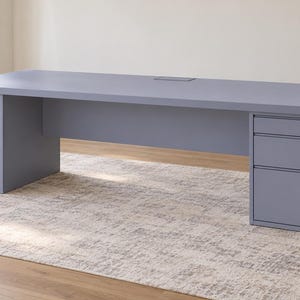 Peut inclure: Un grand bureau exécutif rectangulaire de couleur bleu ardoise, doté d'une surface de travail plane avec un port de gestion des câbles central. Le bureau est soutenu par deux caissons assortis, chacun avec trois tiroirs superposés.
