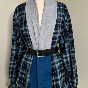 May include: A long-sleeved button-down shirt featuring a blue and black plaid pattern, accented with a wide gray jersey shawl collar and a solid blue vertical panel down the center. The garment is cinched at the waist with a black leather belt.