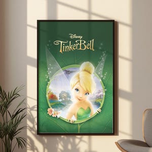 Può includere: Un poster da parete rettangolare incorniciato che presenta il logo Disney Tinker Bell in testo dorato nella parte superiore. L'immagine centrale mostra il personaggio Trilli con capelli biondi e un vestito verde all'interno di una cornice circolare su sfondo a foglia verde.