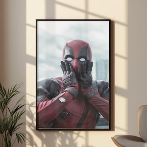 Op de afbeelding: Een ingelijste wandkunstprint met een personage in een rood en zwart tactisch pak met een volledig gezichtsmasker. Het personage heeft witte ooglenzen en houdt beide gehandschoende handen voor het gezicht in een verraste uitdrukking.