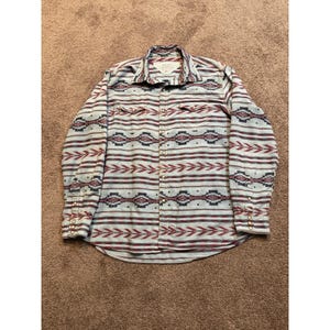 May include: A long-sleeve button-down shirt featuring a light gray base with horizontal stripes in maroon, dark blue, and black. The shirt includes two chest pockets with flaps, a standard collar, and metal snap buttons on the front and cuffs.