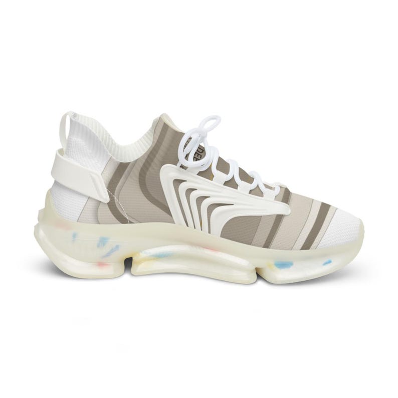 Puede incluir: Una zapatilla baja con parte superior a rayas blancas y beige y cierre de cordones blanco. El calzado incluye un revestimiento estructural blanco en el lateral y una suela gruesa y transl&uacute;cida con motas multicolores incrustadas.