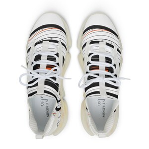 K&ouml;nnte beinhalten: Ein Paar wei&szlig;e Sneaker mit einem schwarzen und orangefarbenen linearen Grafikmuster und Fadenkreuzdetails. Die Schuhe haben wei&szlig;e Schn&uuml;rsenkel, eine durchscheinende Sohle und ein Innenetikett mit der Aufschrift US M 9.5 F 11.5.