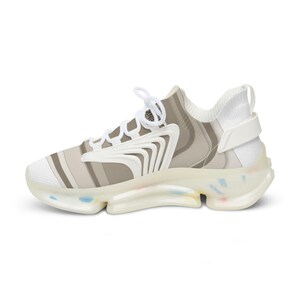 Puede incluir: Una zapatilla baja con un patr&oacute;n de rayas blancas y beige en la parte superior, cordones blancos y una superposici&oacute;n estructural blanca. La suela transl&uacute;cida incluye peque&ntilde;as motas multicolores en la base y el tal&oacute;n.