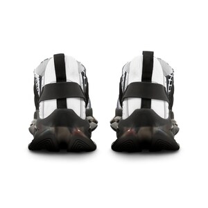 May include: A pair of athletic trainers shown from the back, featuring a white upper with black grid patterns, a black heel strap, and a thick, sculpted black sole with a translucent section. The design includes a black pull tab at the heel.