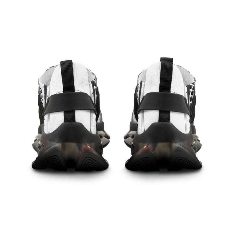 May include: A pair of athletic trainers shown from the back, featuring a white upper with black grid patterns, a black heel strap, and a thick, sculpted black sole with a translucent section. The design includes a black pull tab at the heel.