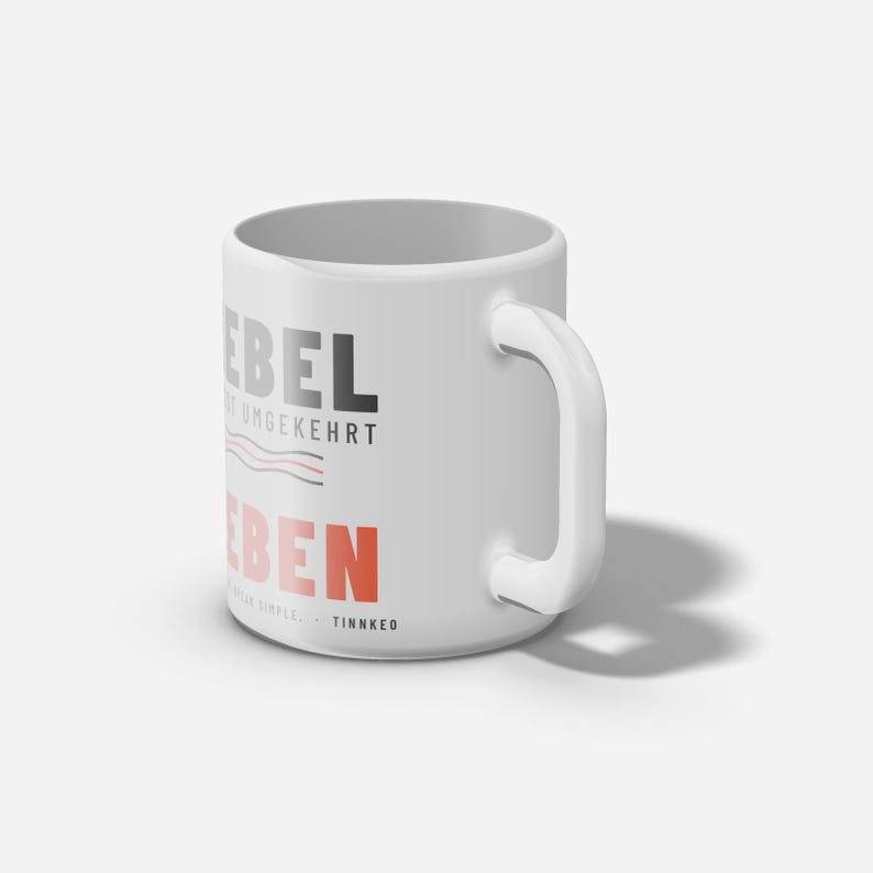 Puede incluir: Una taza de cer&aacute;mica blanca con el texto negro "LEBEL" sobre el texto gris "IST UMGEKEHRT" y el texto rojo "LEBEN". Debajo del texto hay dos l&iacute;neas onduladas y el peque&ntilde;o texto negro "SPEAK SIMPLE. - TINNKEO". La taza tiene un asa.