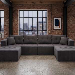 May include: A large, dark gray corduroy sectional sofa featuring a modular design with two extended ottomans, tufted seat cushions, and two matching square throw pillows. The sofa has a low-profile frame and a textured, ribbed fabric finish.