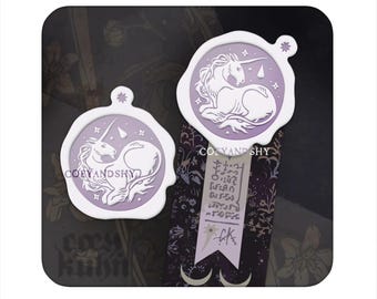 May include: Two white and lavender unicorn wax seals. The seals feature a unicorn design with stars and a teardrop. The seals are on a patterned background with the text "COEYANDSHY".
