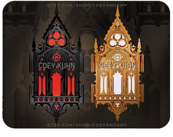 Könnte beinhalten: Zwei architektonische Pins im gotischen Stil, einer schwarz mit roten Akzenten und der andere golden. Beide Pins zeigen den Text "COEY KUHN" und aufwendige Details.