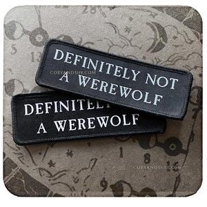 May include: Two black fabric patches with white text. The top patch reads "Definitely Not A Werewolf" and the bottom patch reads "Definitely A Werewolf".