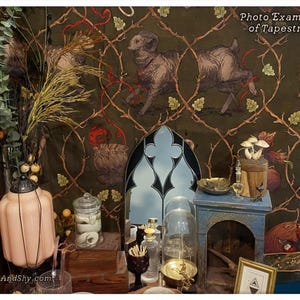 May include: A green tapestry featuring a repeating pattern of branches, leaves, and a ram. The tapestry is hung on a wall with various decorative objects in front of it, including a glass jar, a glass dome, and a small wooden table.
