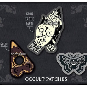 Puede incluir: Tres parches termoadhesivos en blanco y negro con temas ocultos. Los parches representan un par de manos en oraci&oacute;n, una planchette de Ouija y una polilla. El texto "COEY KUHN" aparece en cada parche. El texto "GLOW IN THE DARK!" aparece sobre el parche de las manos en oraci&oacute;n. El texto "GOLD!" aparece sobre el parche de la planchette. El texto "OCCULT PATCHES" aparece debajo de los parches.