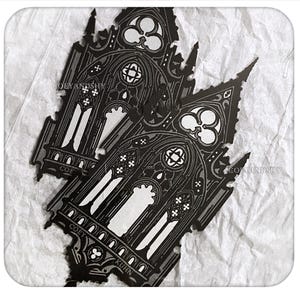 May include: Two black die-cut stickers featuring a detailed architectural illustration of a gothic cathedral window with pointed arches, intricate tracery, and clover-shaped motifs. The text COEYANDSHY and KUHN is printed on the black surface.